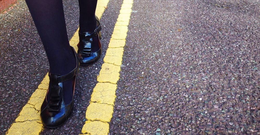 A woman toeing the yellow line on the road.