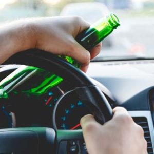A man driving a car with a bottle of beer in his hand.