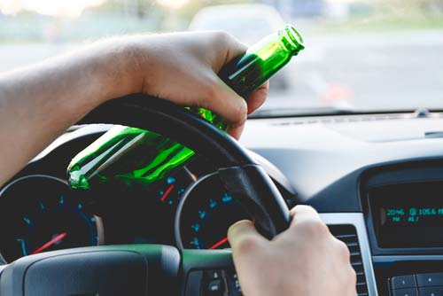 A man driving a car with a bottle of beer in his hand.